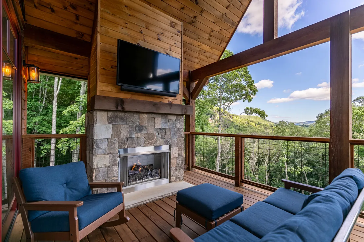 An exterior seating area with a cozy fireplace set against the backdrop of lush natural surroundings. The arrangement invites groups to relax, socialize, and enjoy the evening ambiance outdoors—perfect for winding down after a day of adventure. A television and nature views offer both entertainment and tranquility.