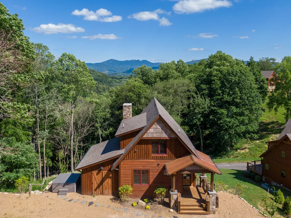 The hero image showcases a charming wooden cabin nestled among lush trees, with sweeping mountain vistas in the distance. The inviting porch overlooks a tranquil landscape, capturing the golden light of sunset and hinting at the peaceful seclusion of the home. There are visible nature trails winding through the property, emphasizing the opportunity for outdoor adventure right outside the door.