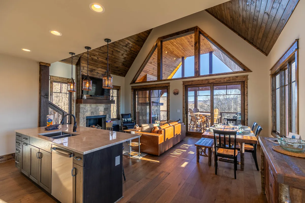 A sweeping view of the open kitchen, dining area, and living space with large windows offering sunrise mountain views. The fireplace sets a cozy ambiance, and the inviting arrangement of furniture encourages gatherings and celebrations.