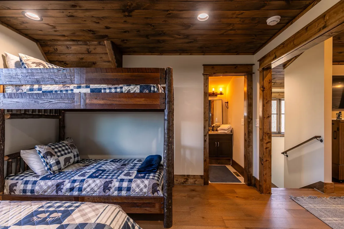 This image focuses on a cozy nook with plaid bunk beds, warm wooden accents, and a view into an adjacent bathroom. The playful bedding and inviting design make it ideal for children or group stays, while the proximity to a bathroom adds convenience.