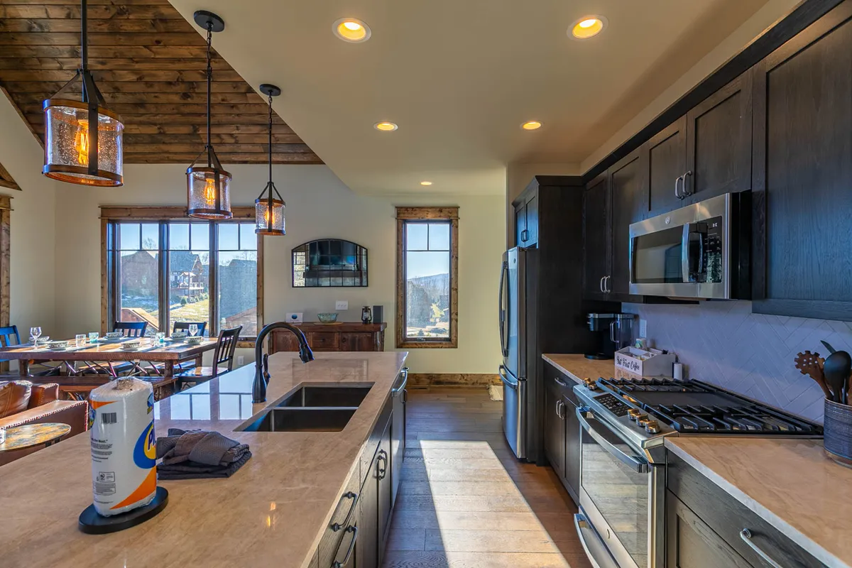 A bright, functional kitchen with a large island, hanging light fixtures, and windows that frame exterior views. The layout suggests a space designed for entertaining, cooking, and hosting guests, with a warm ambience ideal for social events.