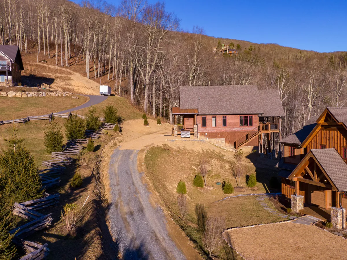 This wide-shot exterior highlights the main house with an adjacent building, surrounded by trees and landscaping. The gravel driveway and open space suggest room for games, outdoor gatherings, and exploration, with a peaceful backdrop ideal for stargazing or enjoying sunsets.